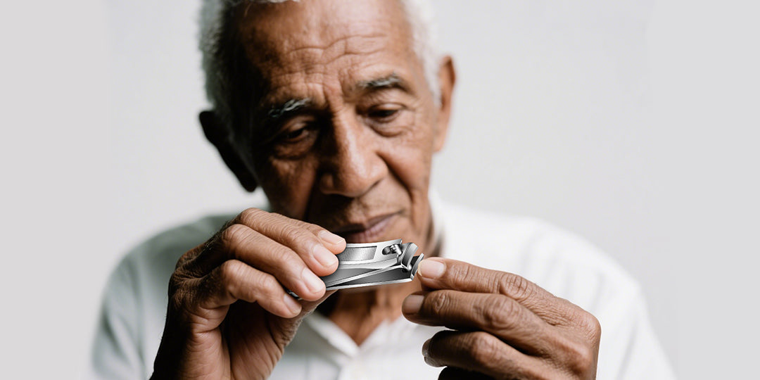Senior man using precision nail clippers for personal grooming on a light background.