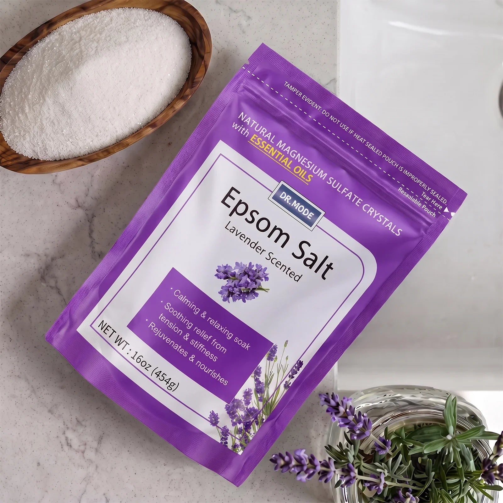 DRMODE Lavender Epsom Salt pouch on a marble counter beside a wooden bowl filled with pure magnesium sulfate crystals and a fresh lavender sprig.