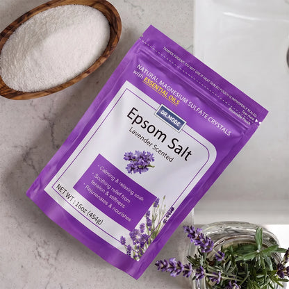 DRMODE Lavender Epsom Salt pouch on a marble counter beside a wooden bowl filled with pure magnesium sulfate crystals and a fresh lavender sprig.