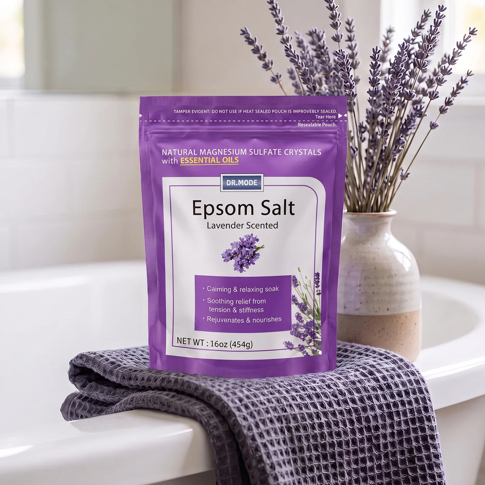 DRMODE Lavender Epsom Salt pouch displayed on a waffle towel in a bright bathroom with a vase of fresh lavender sprigs behind it.