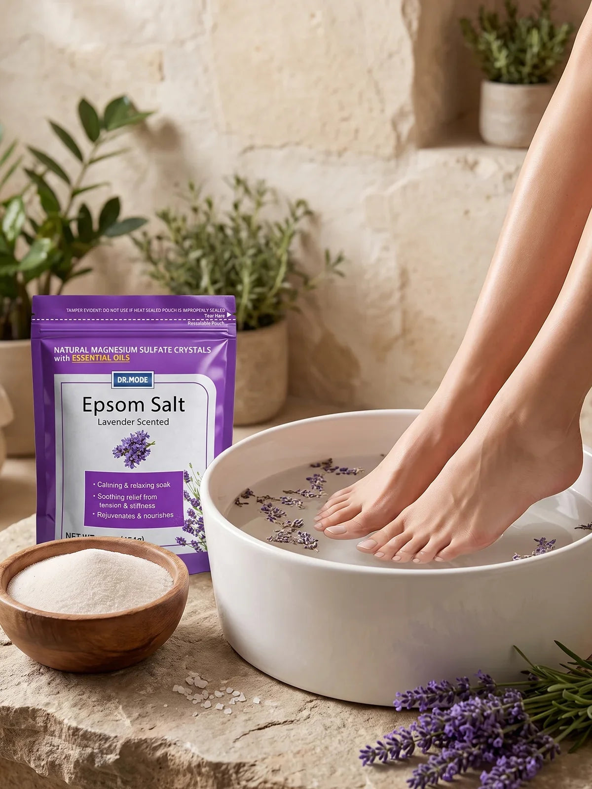 A woman's bare feet soaking in a white bowl of warm water with lavender petals, beside a DRMODE Epsom Salt pouch — a soothing ingrown toenail soak in progress.